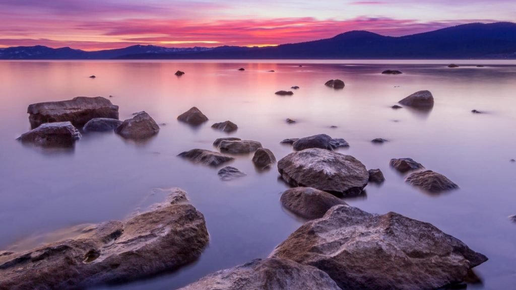 A lake at dusk with many individual stones jutting out of the water.
